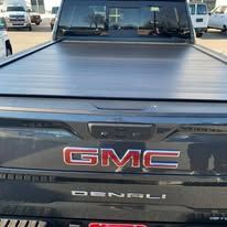 Close-up of a black GMC truck bed with a retractable cover. The GMC logo is visible.