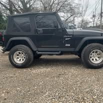 Black Jeep Wrangler parked outdoors on a gravel surface.