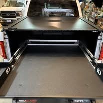 Black truck bed with a retractable bed cover extended, in an outdoor setting.