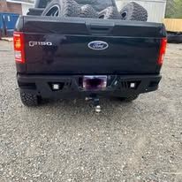 Black Ford truck rear with custom bumper and spare tires.