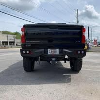 Black pickup truck rear view with custom bumper parked on pavement.