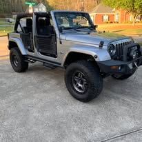Silver Jeep with black rims parked on pavement.