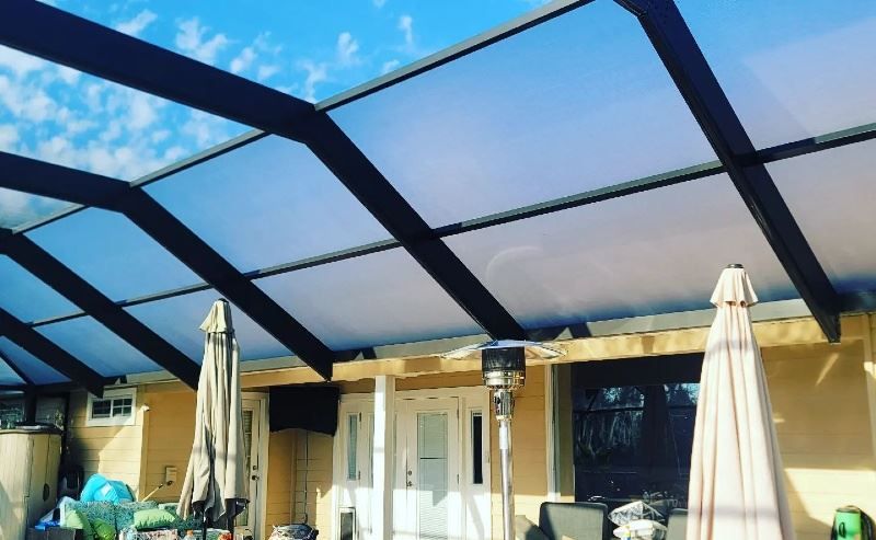 A patio with umbrellas and a heater under a clear roof.