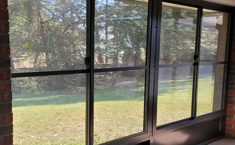 A screened in porch with a lot of windows and a brick wall.