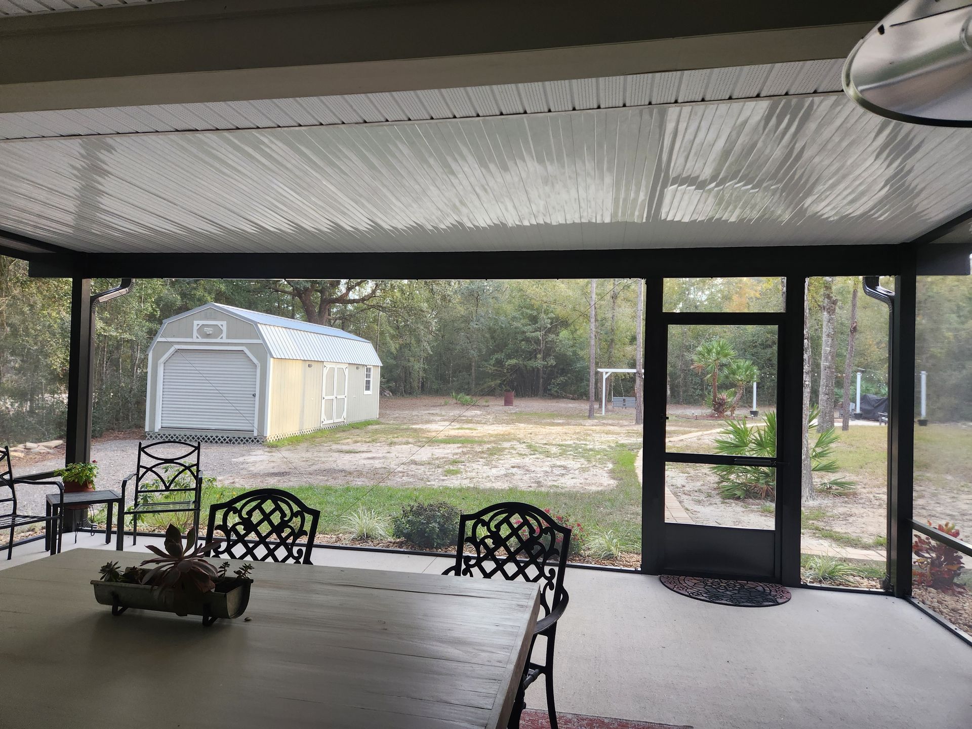 A screened in porch with a table and chairs and a shed in the background.