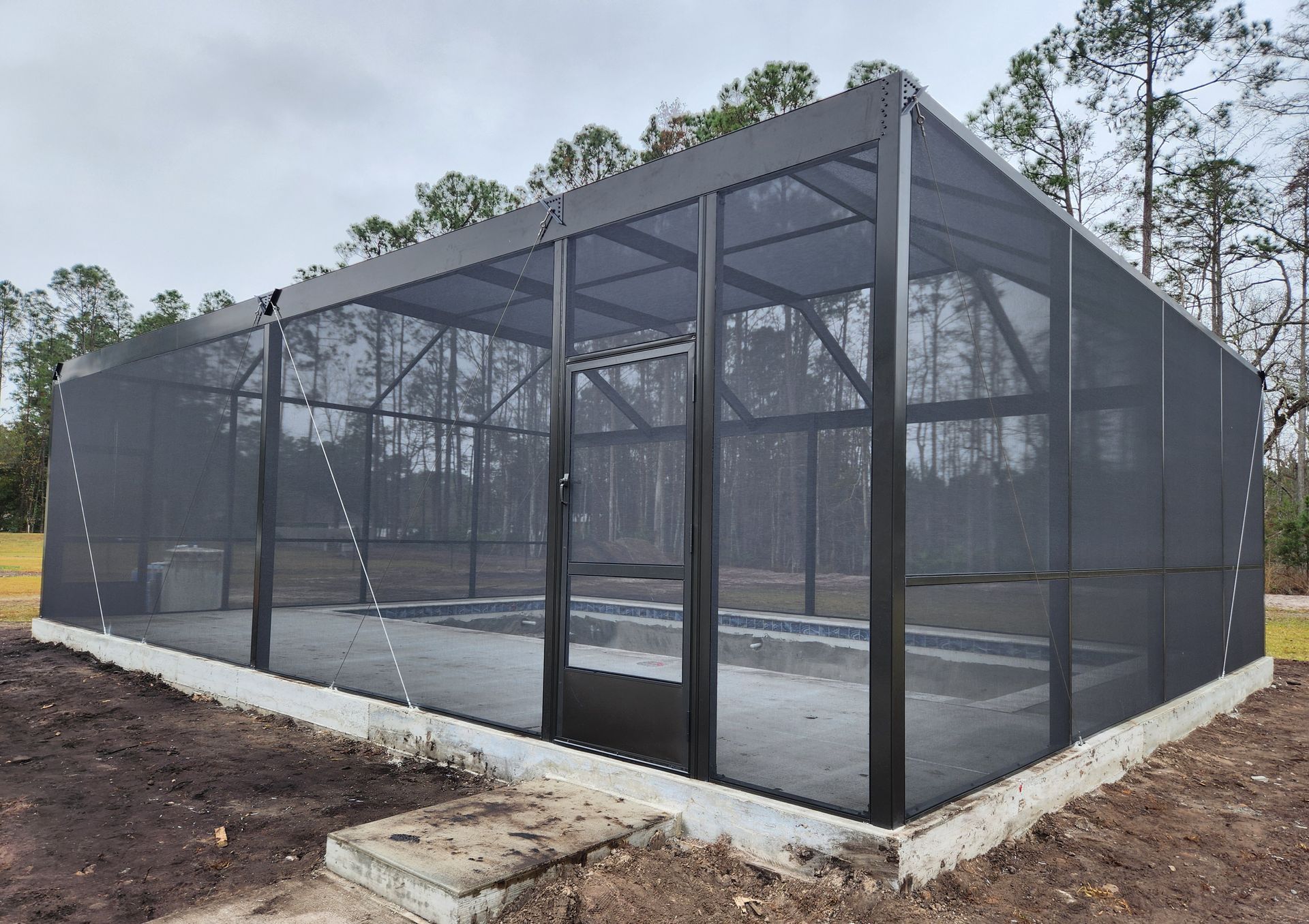 A large screened in swimming pool with trees in the background.