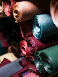 Rolls of colorful leather stacked on a shelf, varying shades of red, blue, green, and tan.