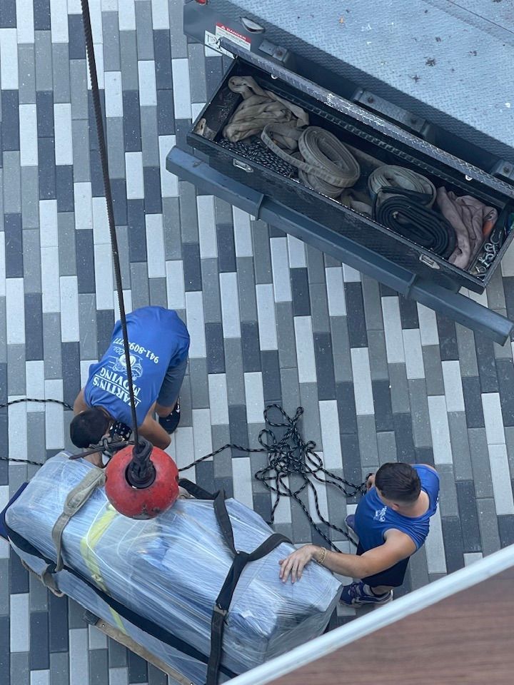 Workers using a crane to lift a large, wrapped object, likely furniture, from the ground.
