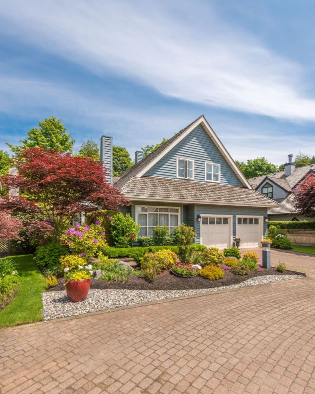 Charming house with gray roof, flowering garden, and brick driveway under a blue sky