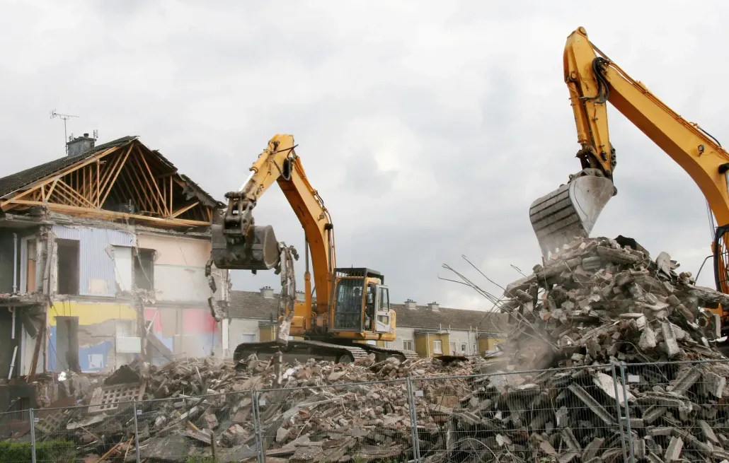 Excavators clearing rubble from a demolished building on a construction site under cloudy skies.