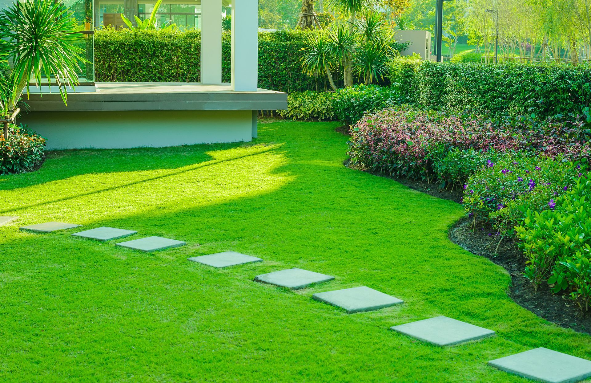 Lush green garden lawn with stepping stones, hedges, and a shaded patio bench area