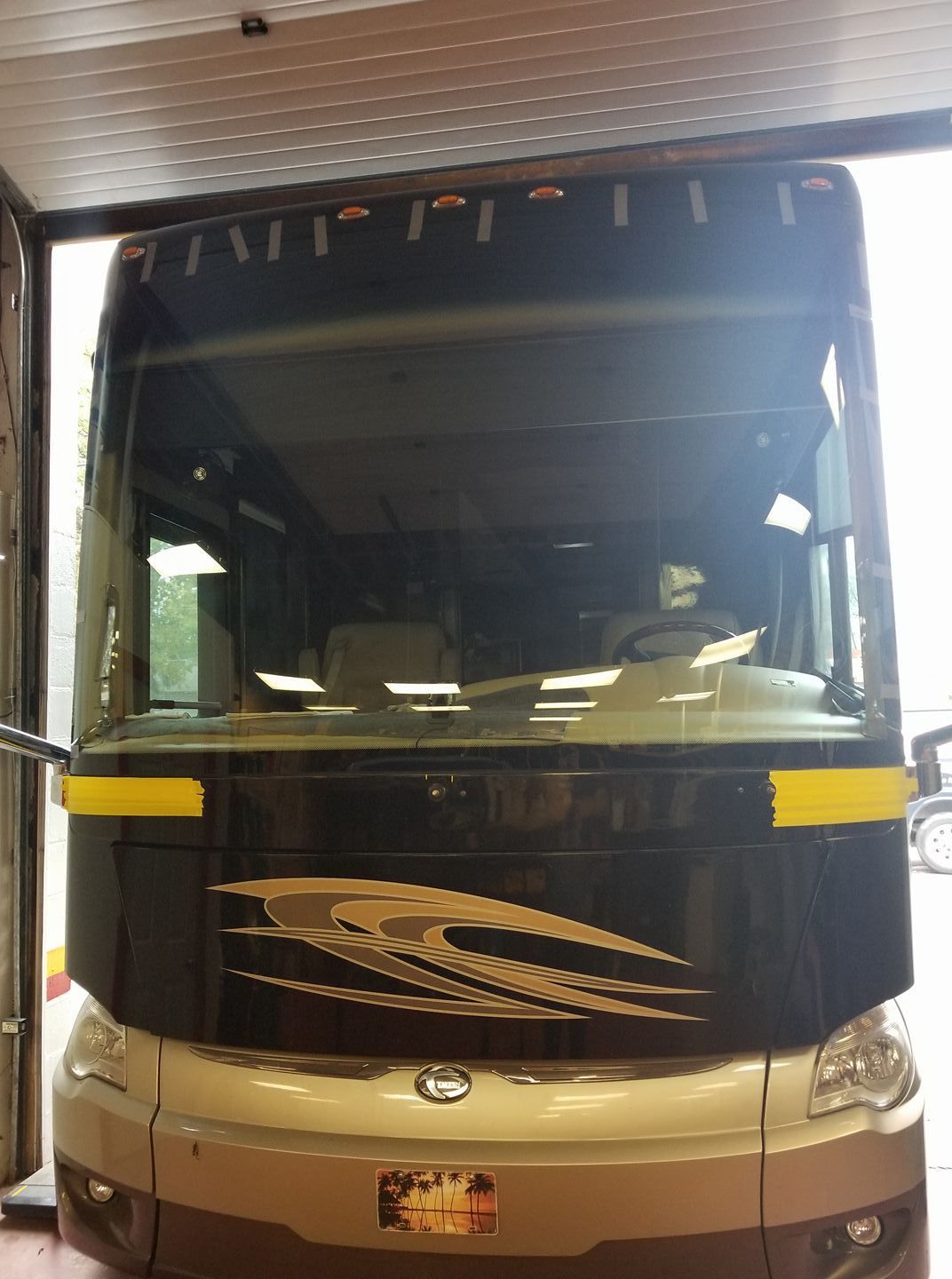 Large coach bus parked indoors, front view with black and beige body and yellow side stripes.