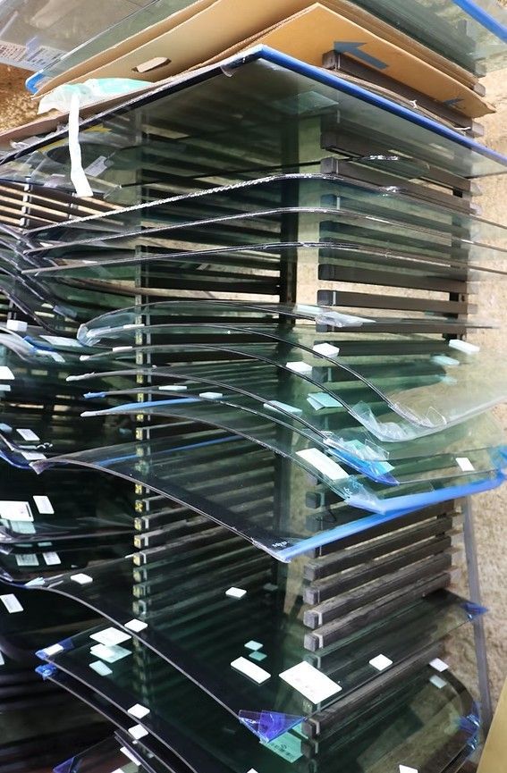 Stacks of glass shelves or panels in a warehouse, with green-tinted edges and cardboard above.