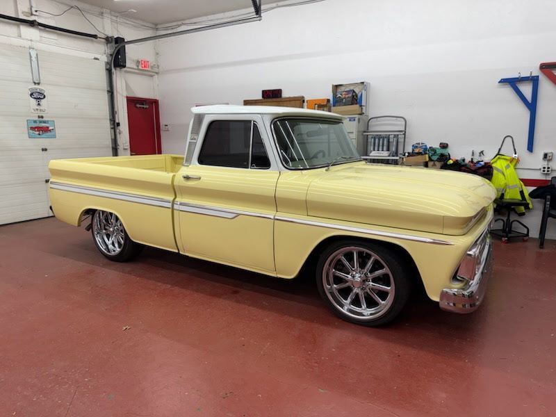 Yellow classic pickup truck parked in a garage with a red floor.