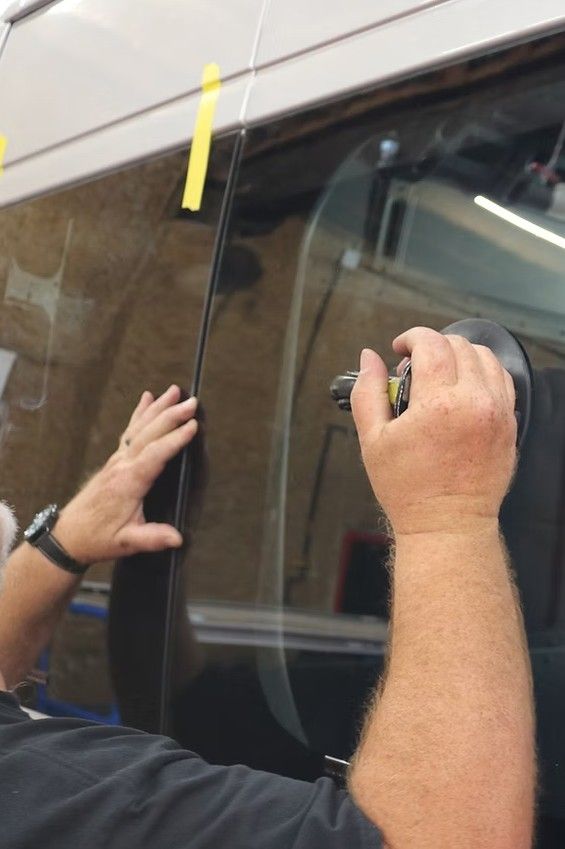 Person applying black tape to a vehicle window with a yellow strip marker above it