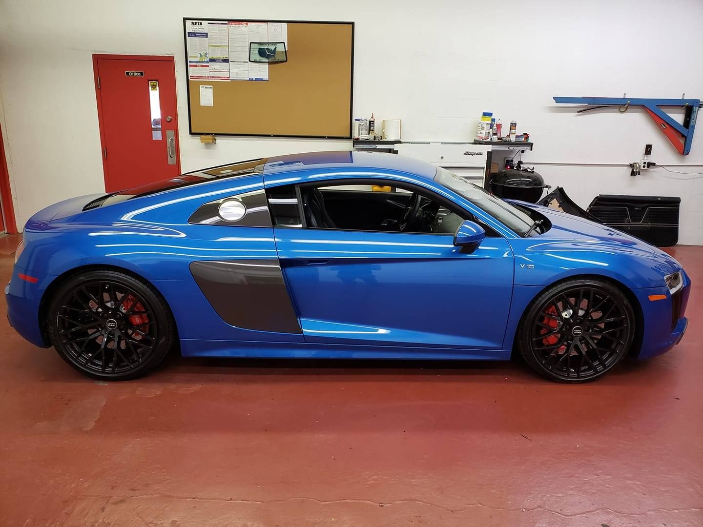 Blue sports car in a garage, viewed from the side, with black wheels and a red floor.