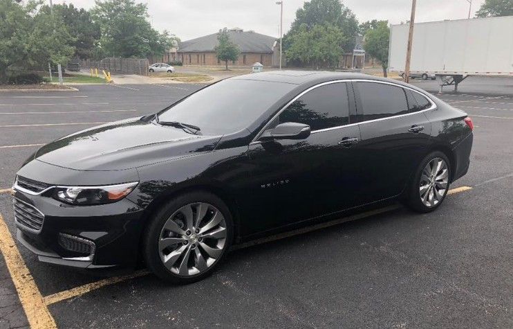 Black sedan parked in a wet lot with tinted windows and silver rims.