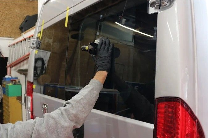 Gloved worker applying film to a van’s rear window in a workshop.