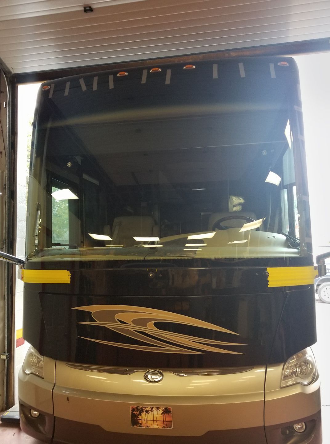 Front view of a beige and black bus parked indoors under a metal roof.