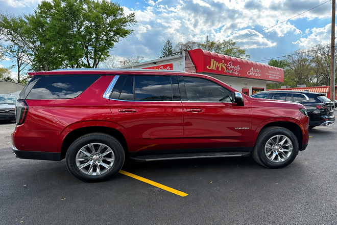 Red SUV parked in a lot, with a red-roofed building and trees in the background.