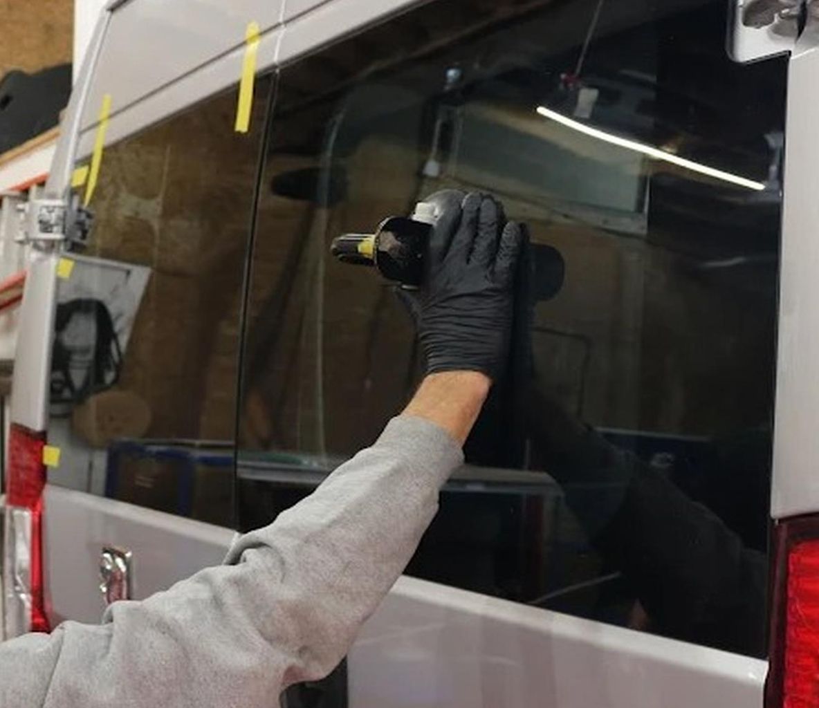 Gloved hand using a suction tool to apply tint film to a vehicle window.