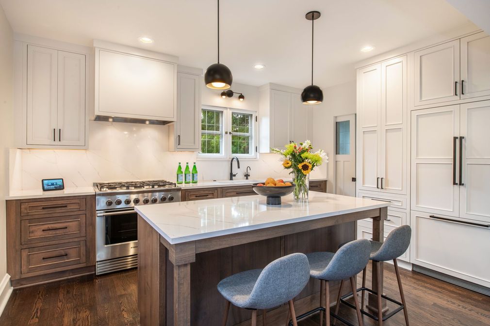 A bright modern kitchen with white cabinets, a large central wooden island, three blue stools, and hanging pendant lights.