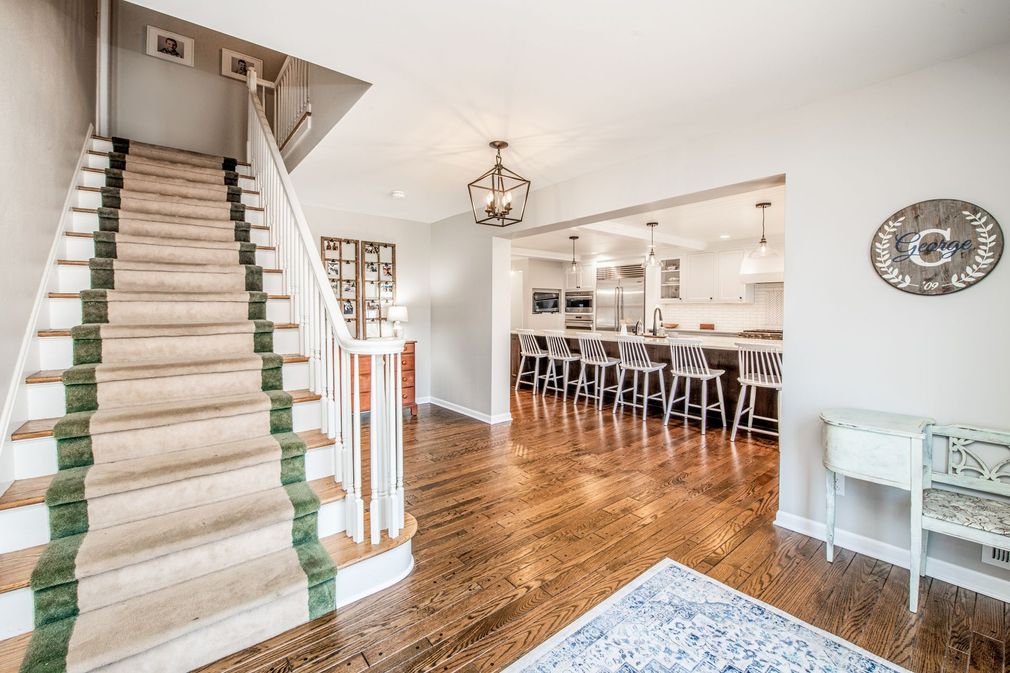 A staircase with a beige runner and green trim leads to an open kitchen with a breakfast bar on hardwood floors.