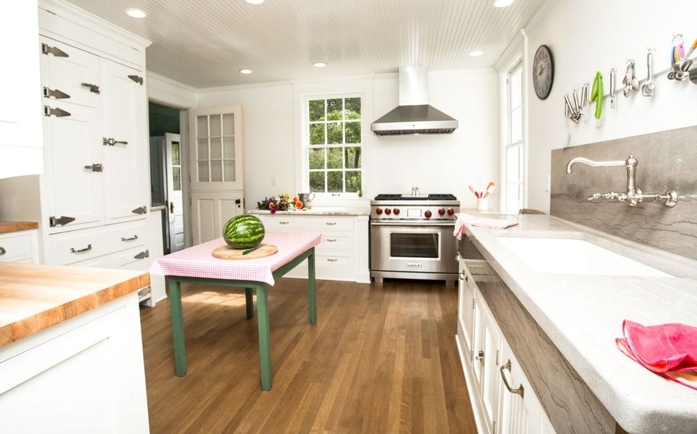 Bright kitchen with white cabinetry, wood flooring, a central island with a watermelon, and a stainless steel stove.
