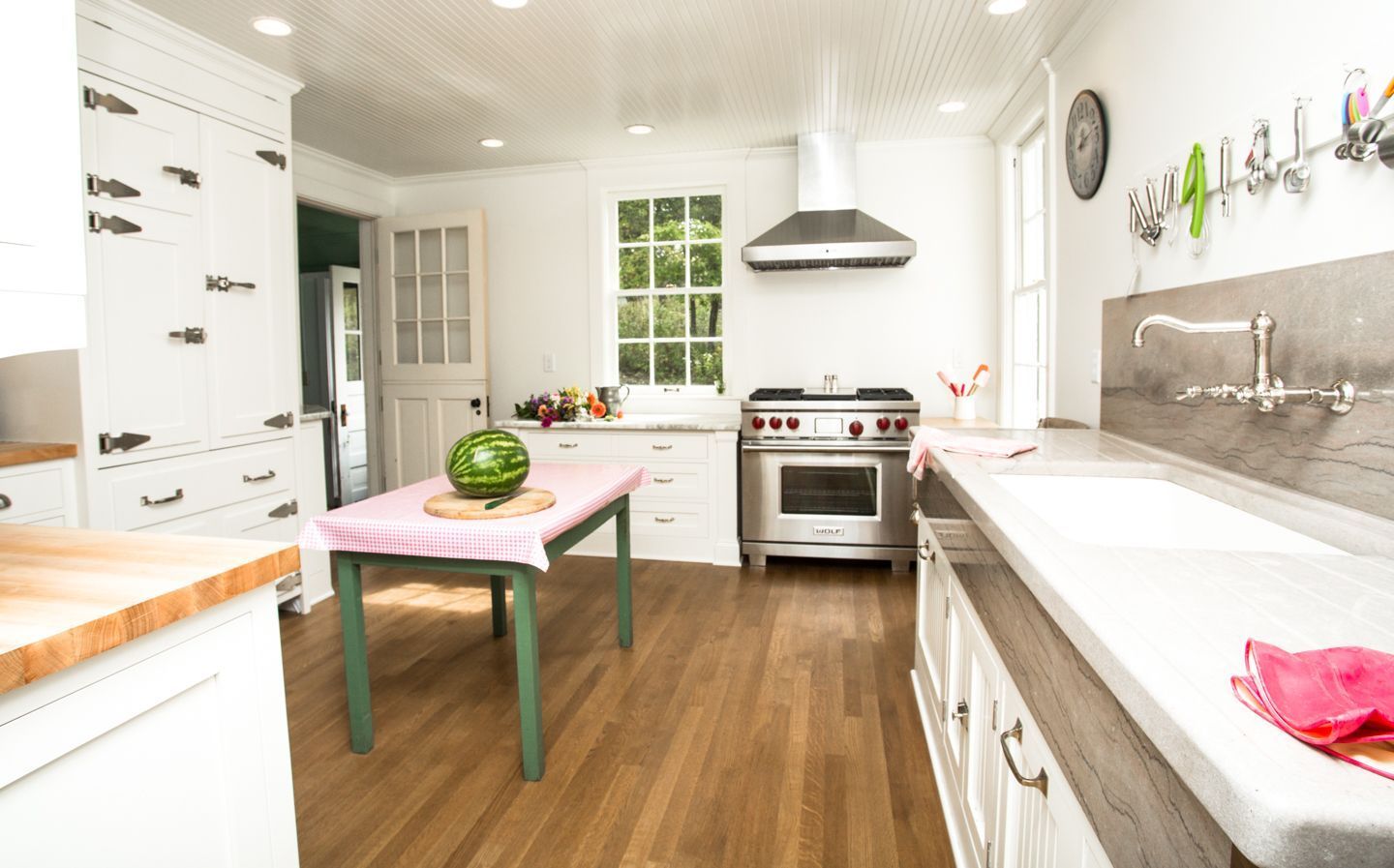 Bright kitchen with white cabinetry, wood flooring, a central island with a watermelon, and a stainless steel stove.