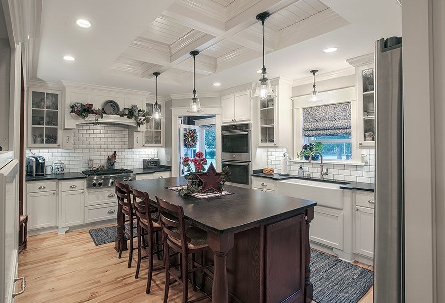 Spacious white kitchen with dark island and stools, overhead lights, and white tiled backsplash.