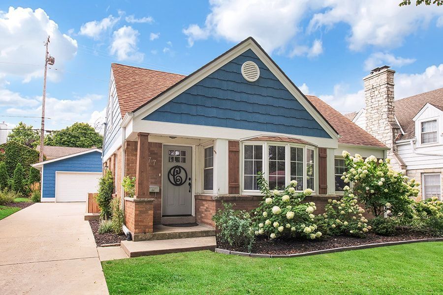 Charming blue cottage with a brown roof, brick accents, and lush green lawn on a sunny day.