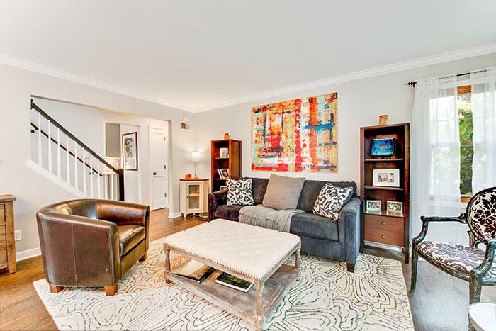 Living room with brown leather chair, sofa, abstract art, and bookshelves on hardwood floor.