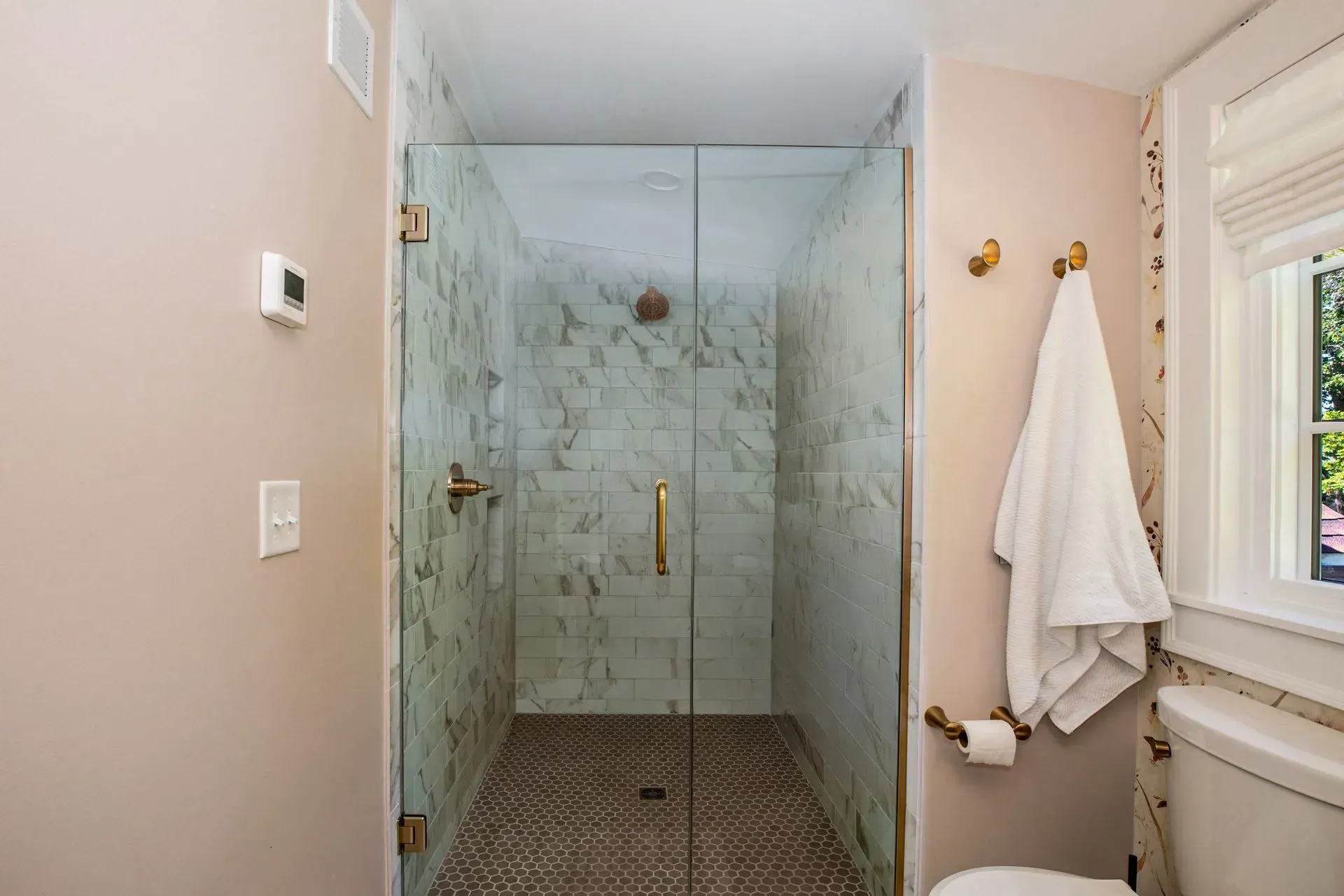 Shower stall with glass doors and marble tile in a blush-toned bathroom, gold hardware.