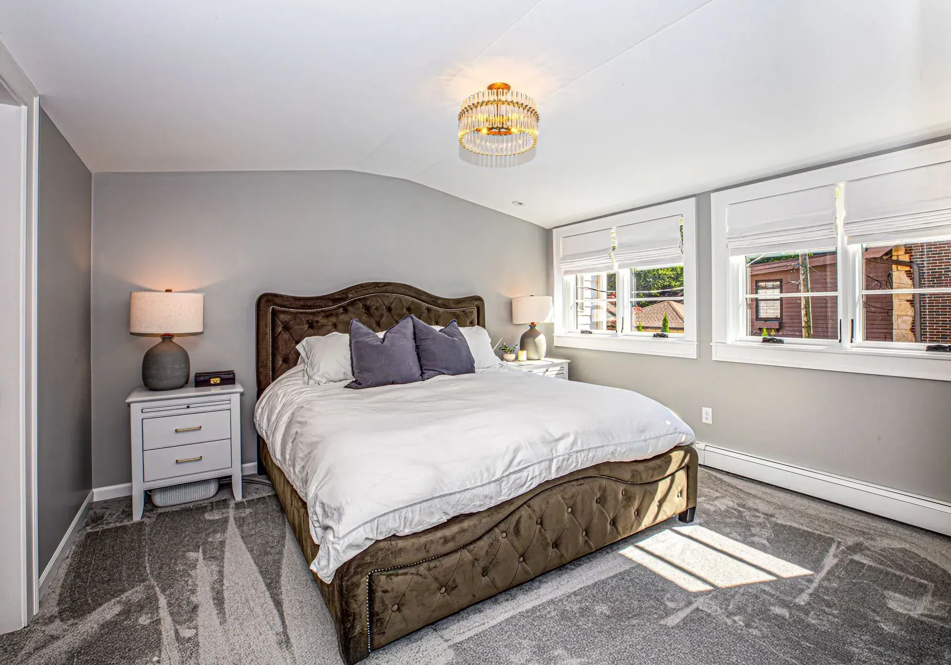 Bedroom with a gray carpet, bed, two bedside tables, and windows.