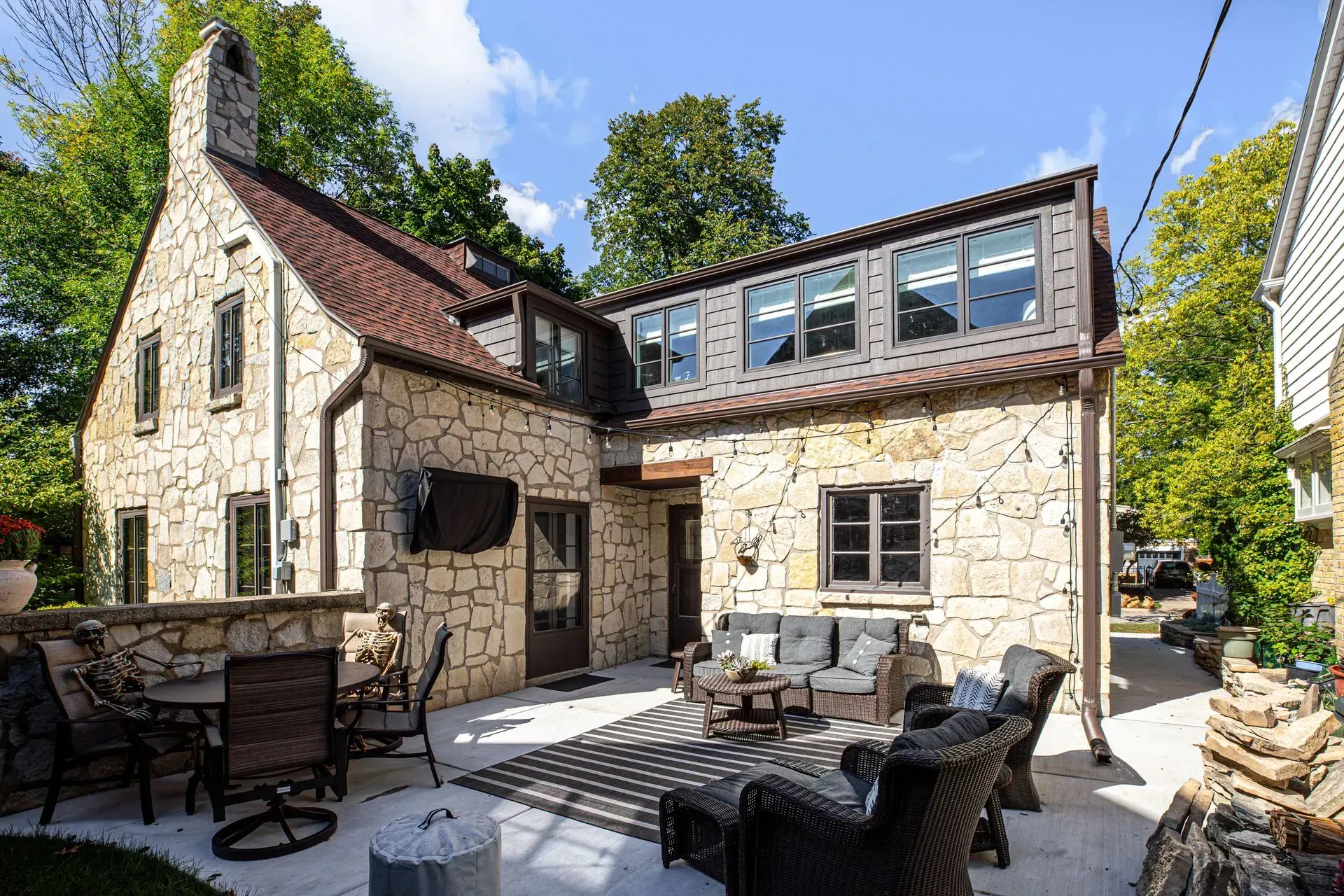 Stone house with outdoor seating area and a modern extension with multiple windows.