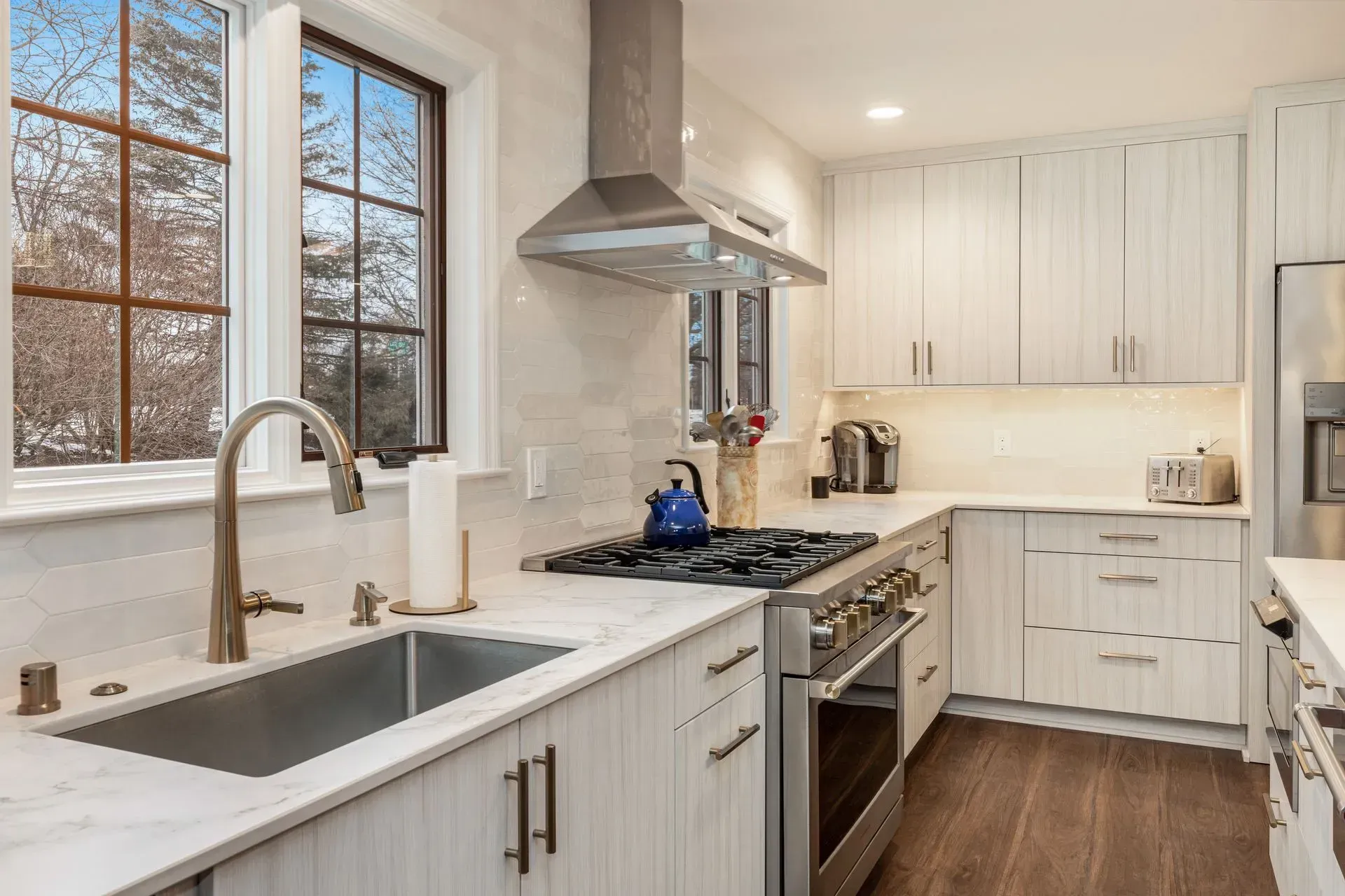 Bright white kitchen with stainless steel appliances and a large window.