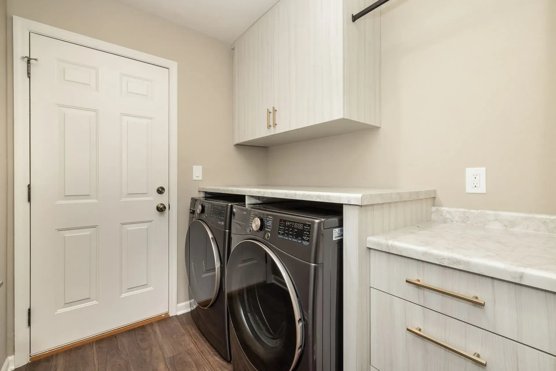 Laundry room with a washing machine, dryer, cabinets, and door.