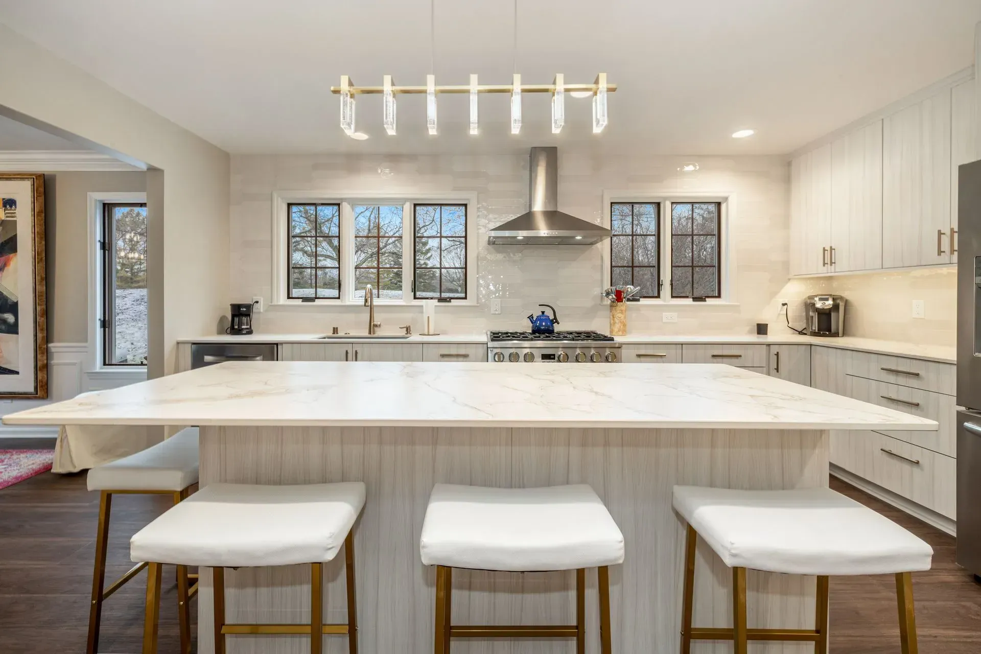 Modern kitchen with island, white cabinets, marble countertop, and bar stools.