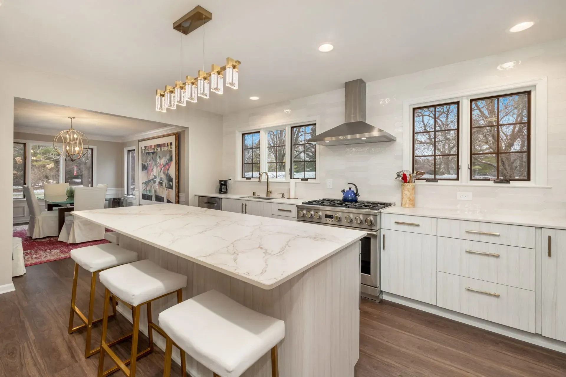 Modern white kitchen with island, stainless steel appliances, and adjacent dining area.