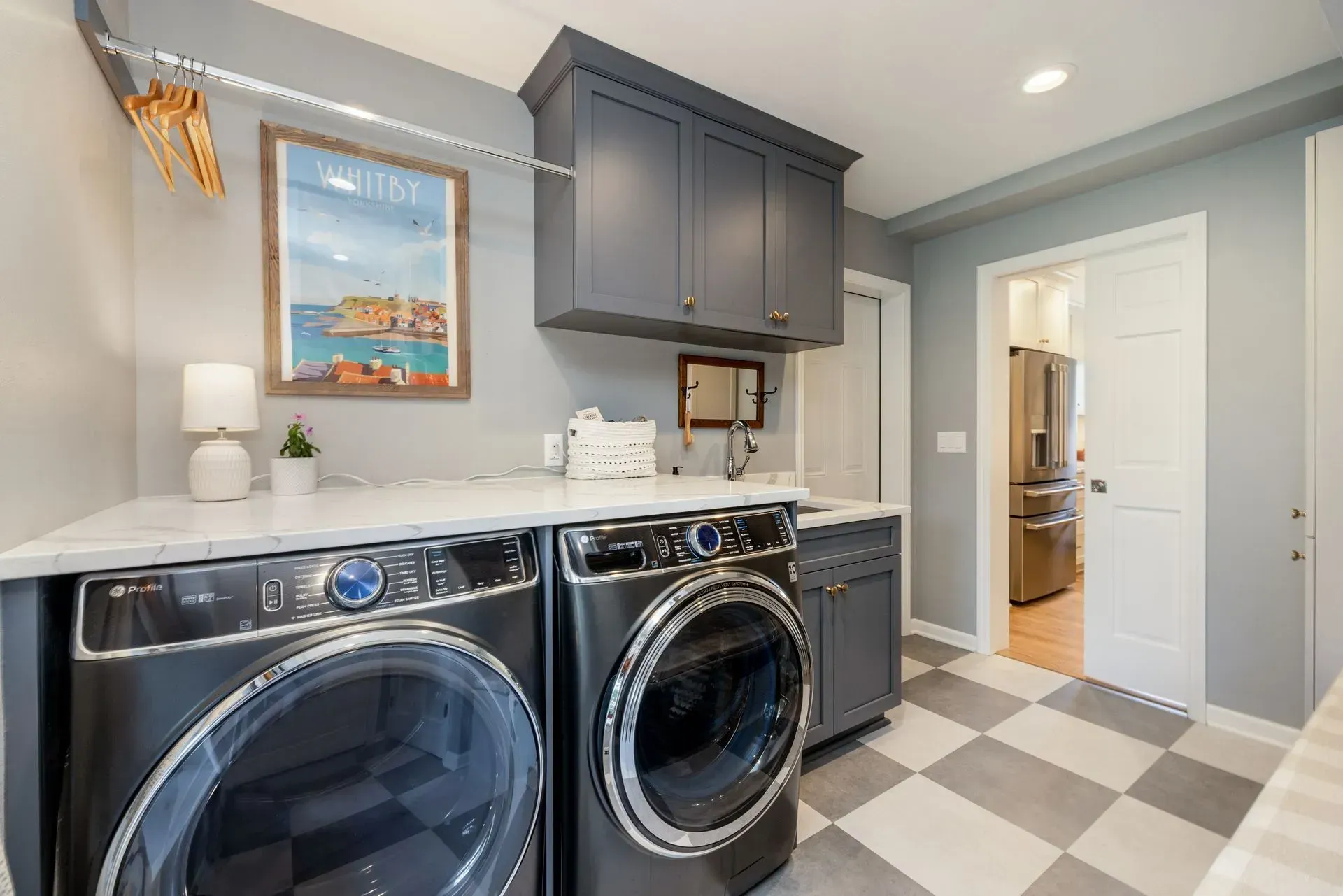 Modern laundry room with gray cabinets, marble countertop, washer/dryer, and checkered floor.