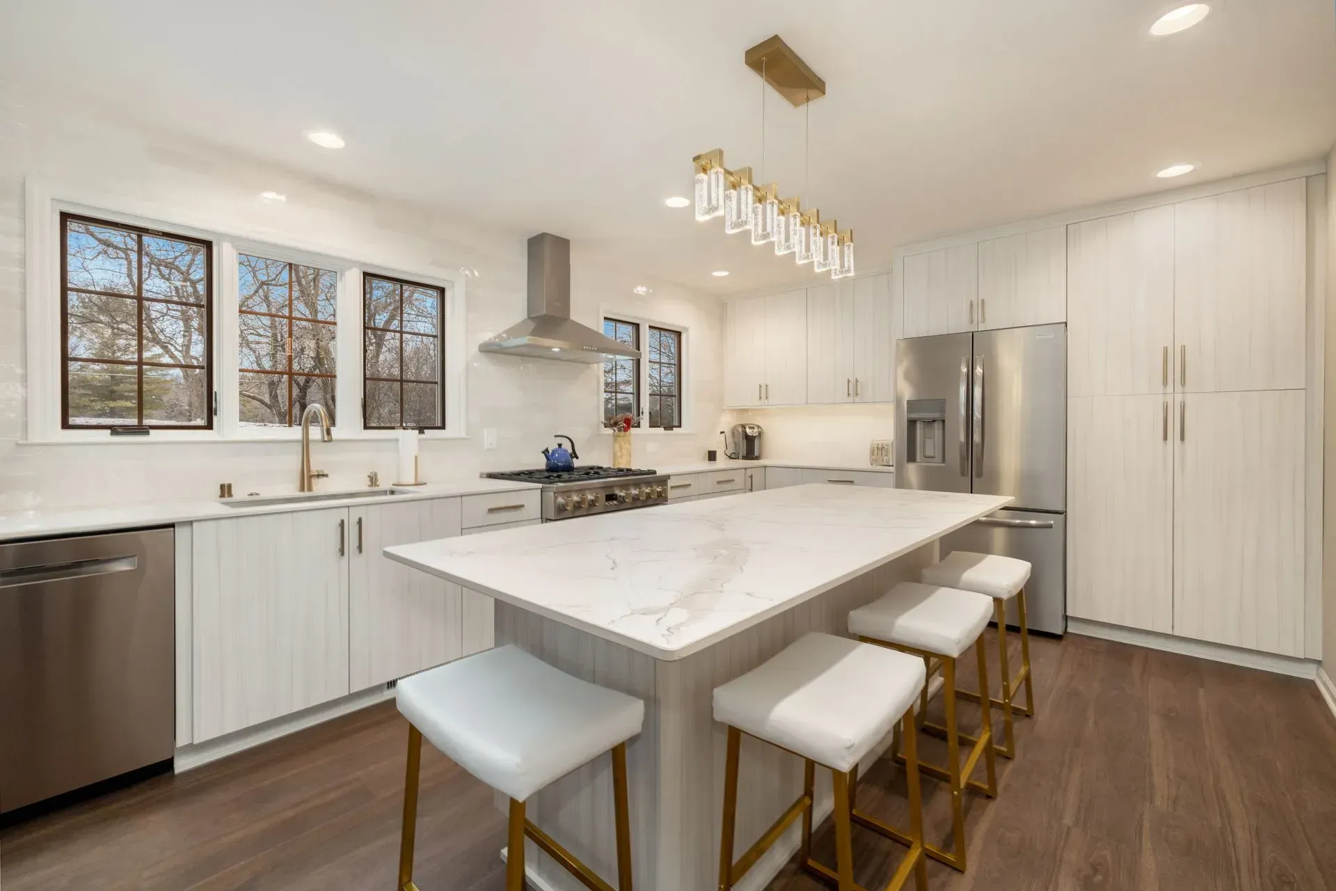 Modern white kitchen with island, stainless steel appliances, and hardwood floors.