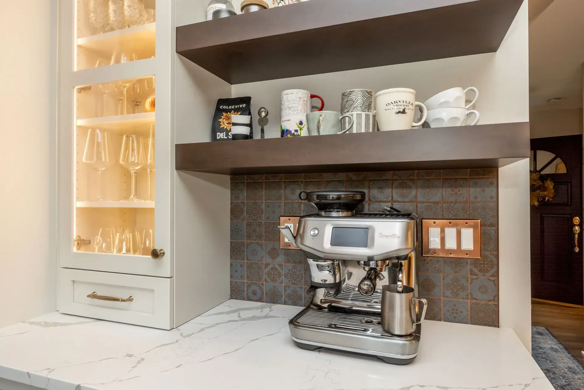 Coffee station with espresso machine, mugs, and shelves in a kitchen.