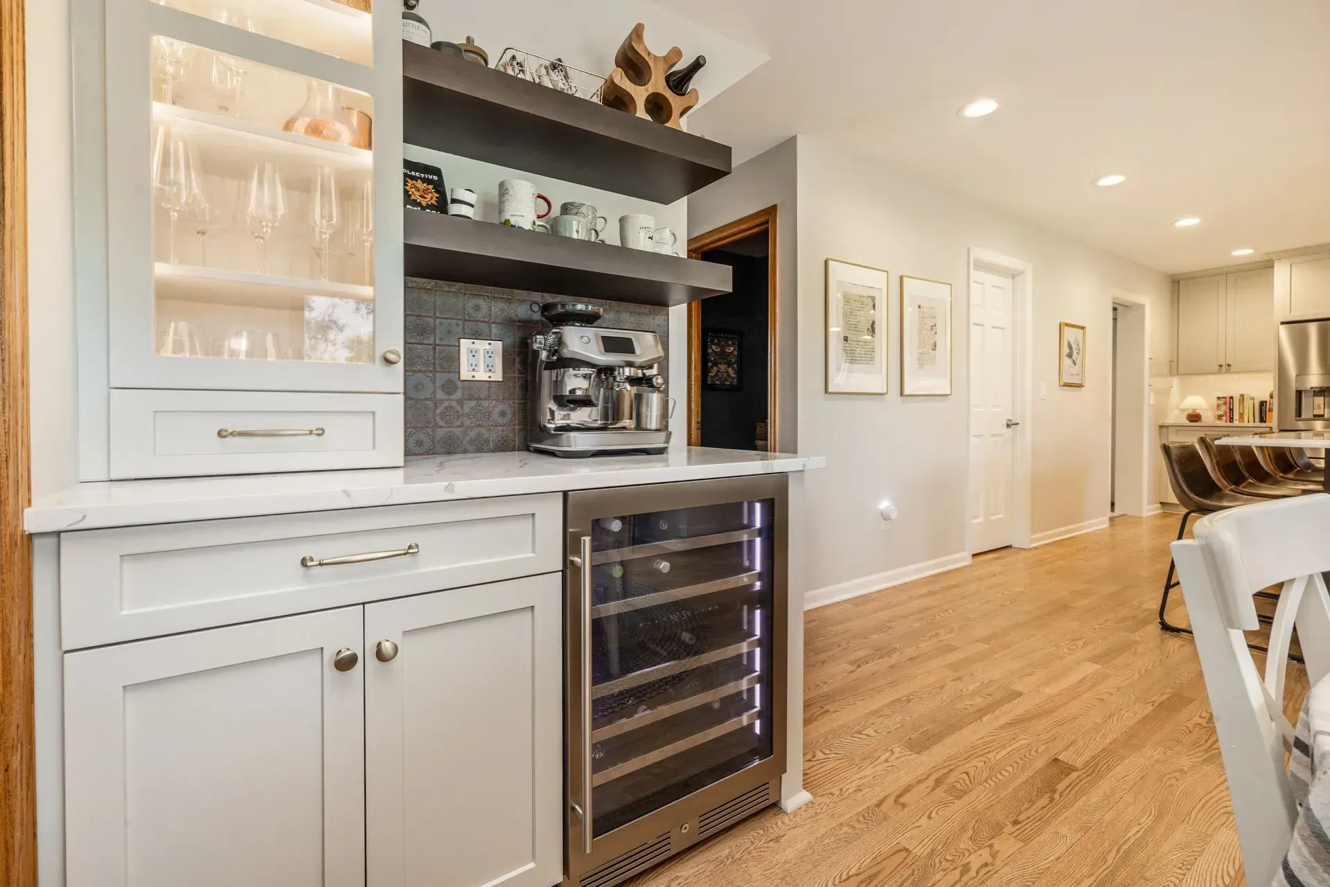 Built-in home bar with wine fridge, espresso machine, glass cabinets, and open shelves against a gray wall.