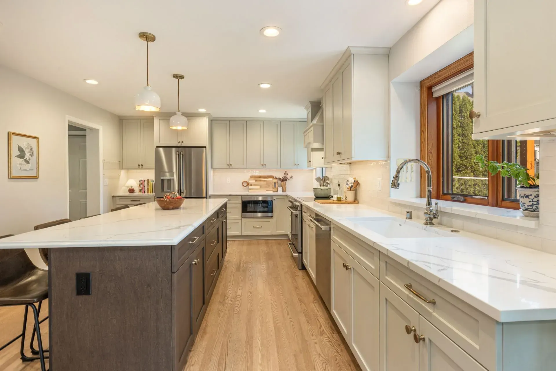 Modern kitchen with light wood floors, white countertops, and gray cabinets. Island with dark brown cabinets.