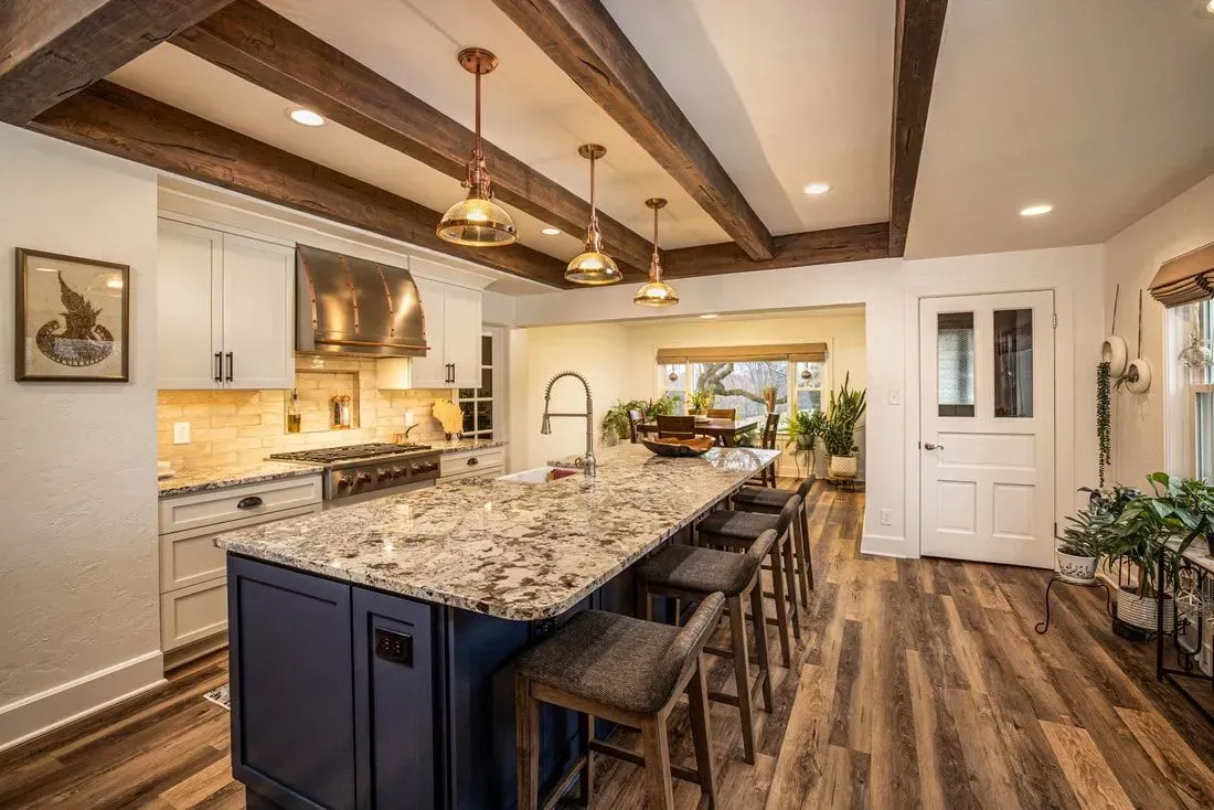 Kitchen with blue island, granite countertop, wooden beams, and pendant lights. Wooden flooring.