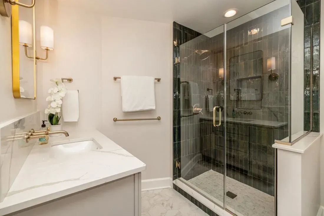 Elegant, modern bathroom with white vanity, glass shower, and gold accents.