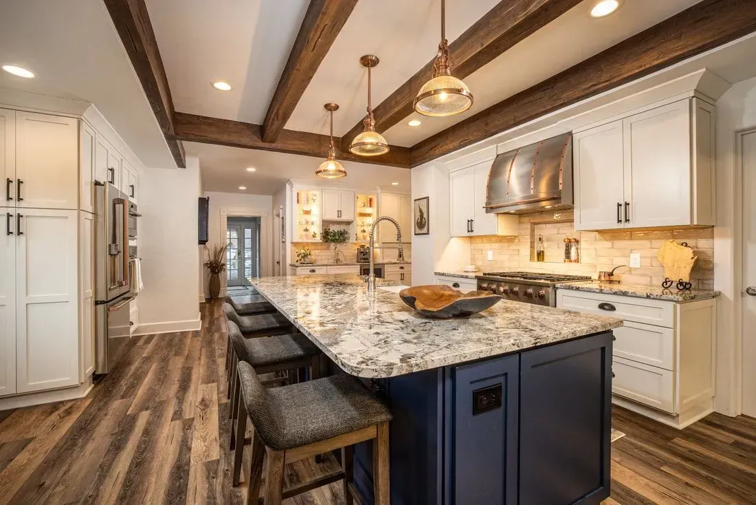 Kitchen with a navy island, white cabinets, wood beams, and gray countertops.