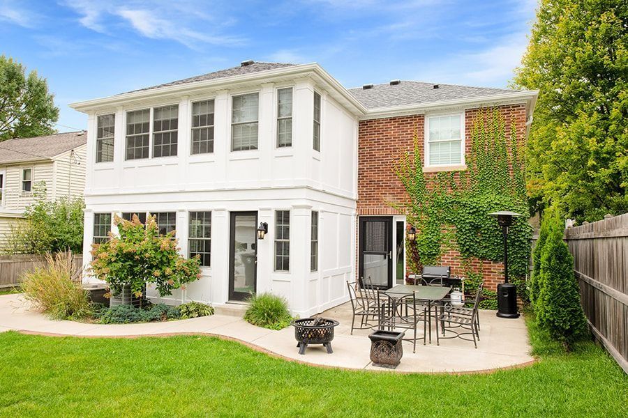 Backyard of a two-story house with patio, grill, and green lawn.