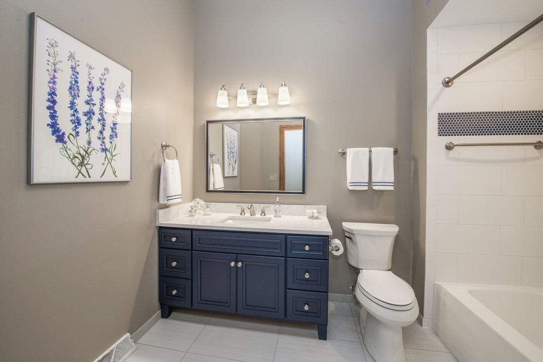 Blue vanity bathroom with white fixtures, blue and white accent tile, and art of blue flowers.