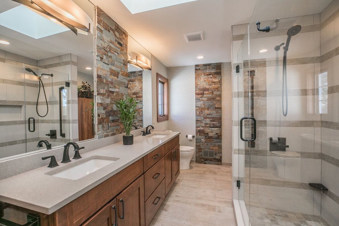 Bathroom with brick accents, dual vanity, glass shower, and skylight.